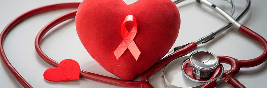 Um coração vermelho com um laço vermelho ao lado de um estetoscópio. O laço vermelho é um símbolo da luta contra a AIDS.